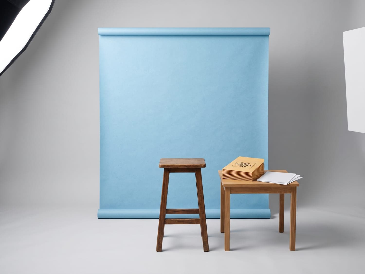 Fond bleu ciel et tabouret d'un poste de portrait scolaire, pochettes de tirages posées à côté.